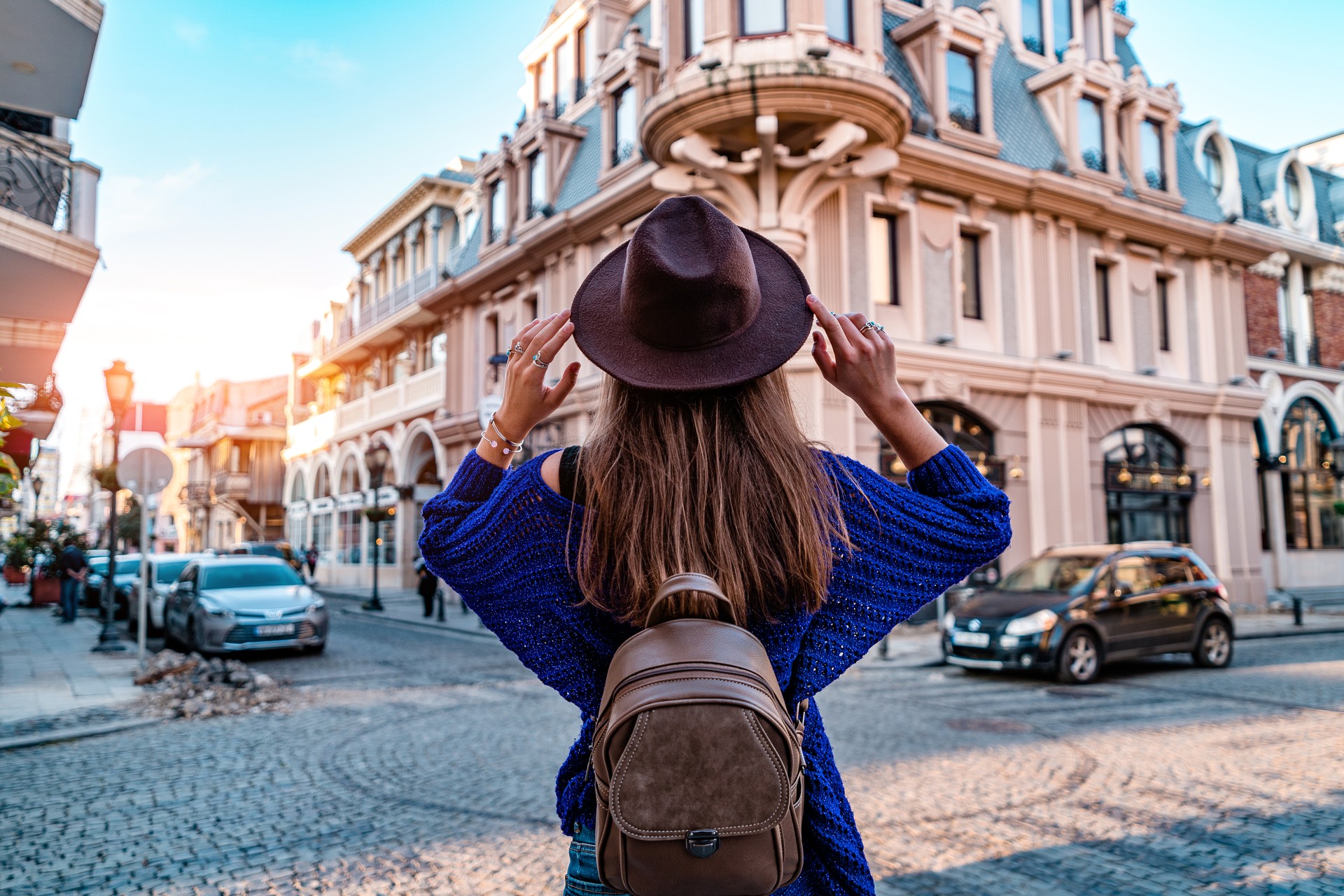 Casual stylish fashionable hipster traveler woman in hat and with brown backpack walking alone around european city